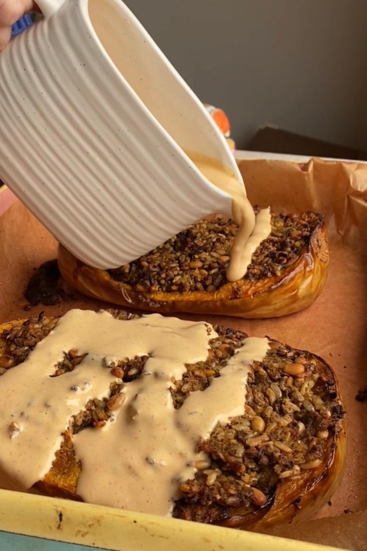 Creamy tahini sauce being poured over baked stuffed butternut squash.
