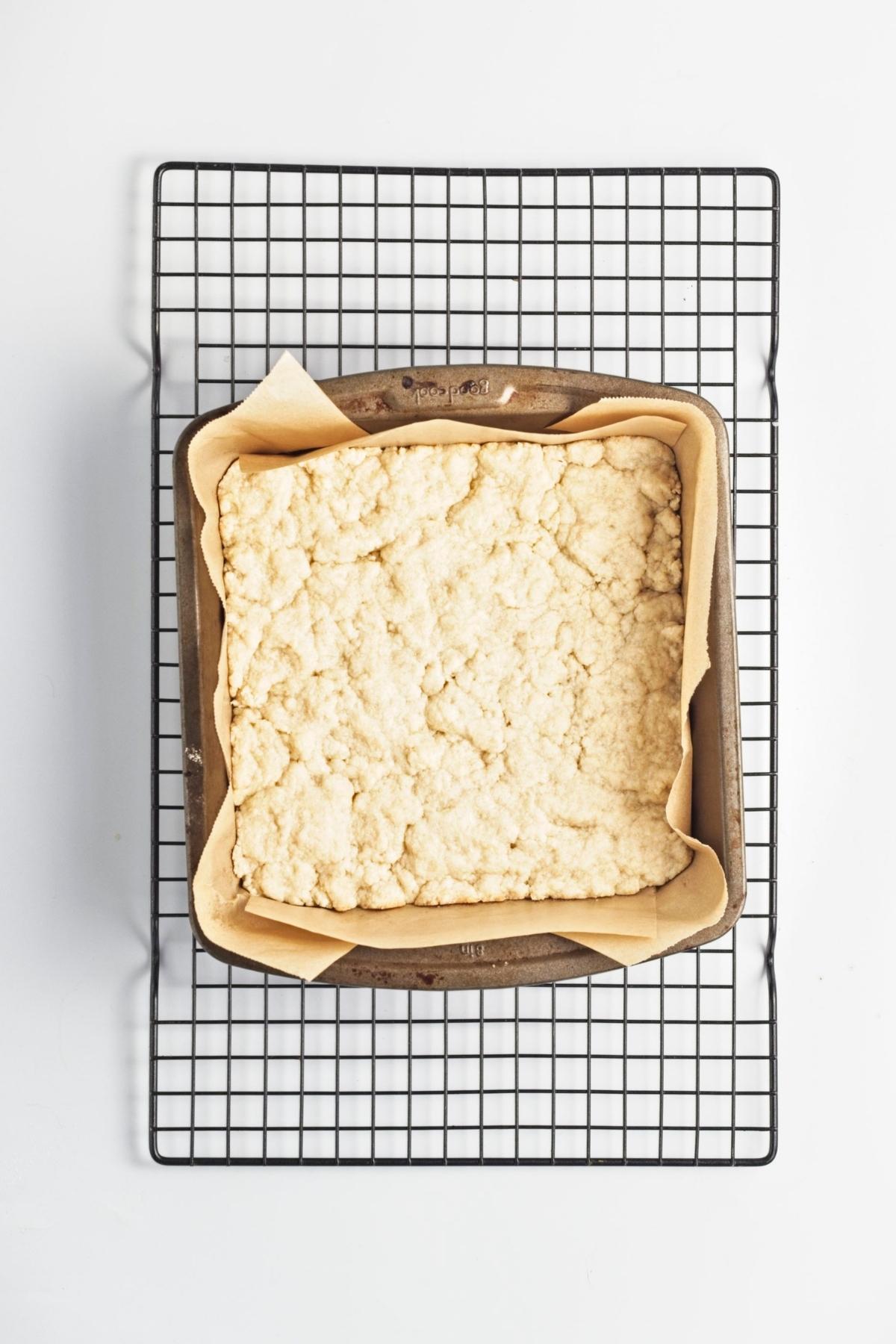 Pressed crust baked in a parchment-lined square pan on a cooling rack.