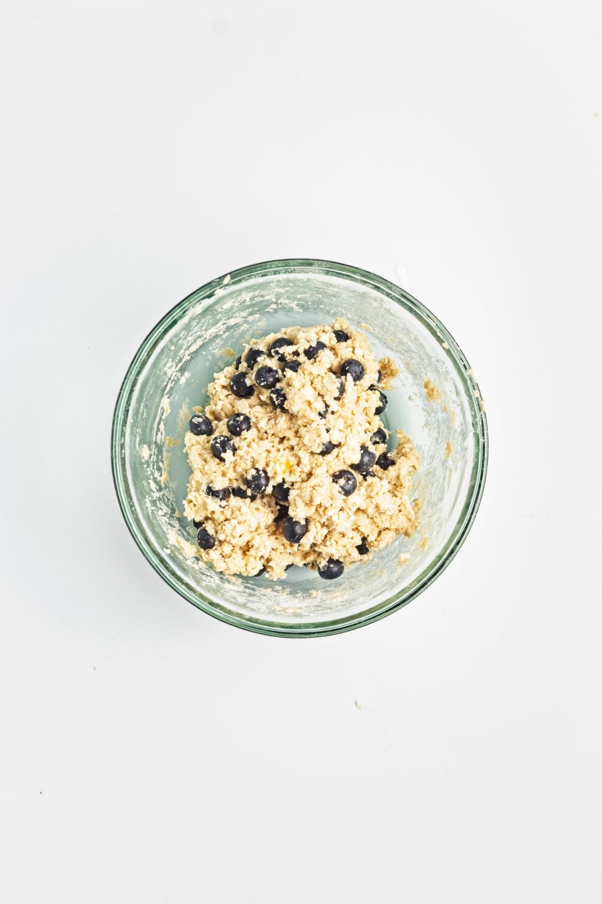 Blueberries folded into thick scone dough in a glass bowl.