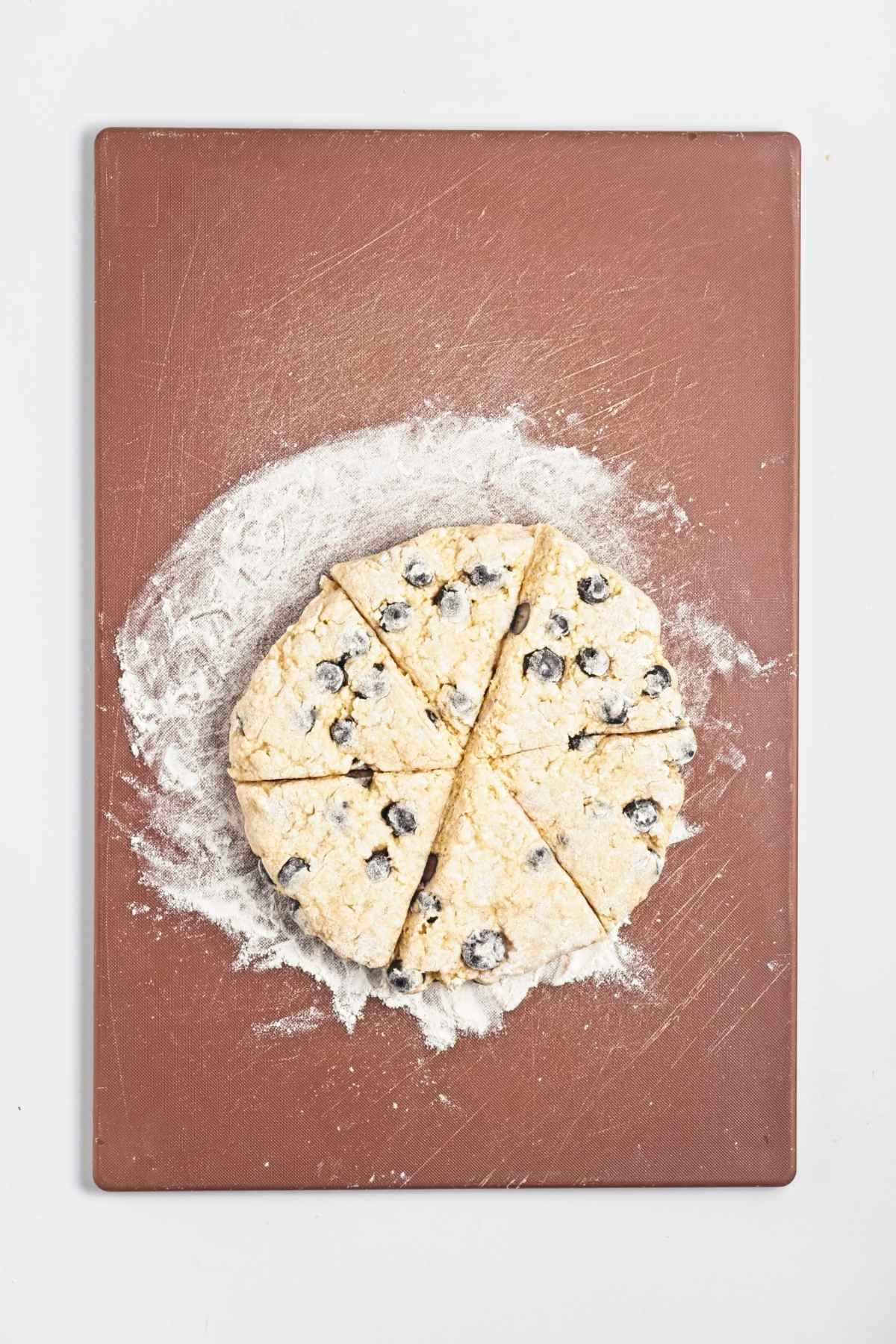 Blueberry scone dough shaped into a round and cut into wedges on a floured board.