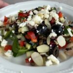 Black lentil salad with cucumber, red pepper, olives, feta, and sliced almonds on a white plate.