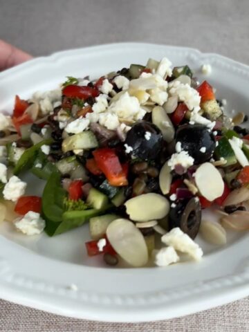Black lentil salad with cucumber, red pepper, olives, feta, and sliced almonds on a white plate.