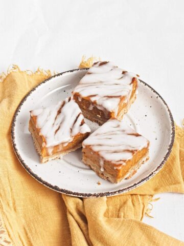 Three glazed pumpkin bars served on a plate.