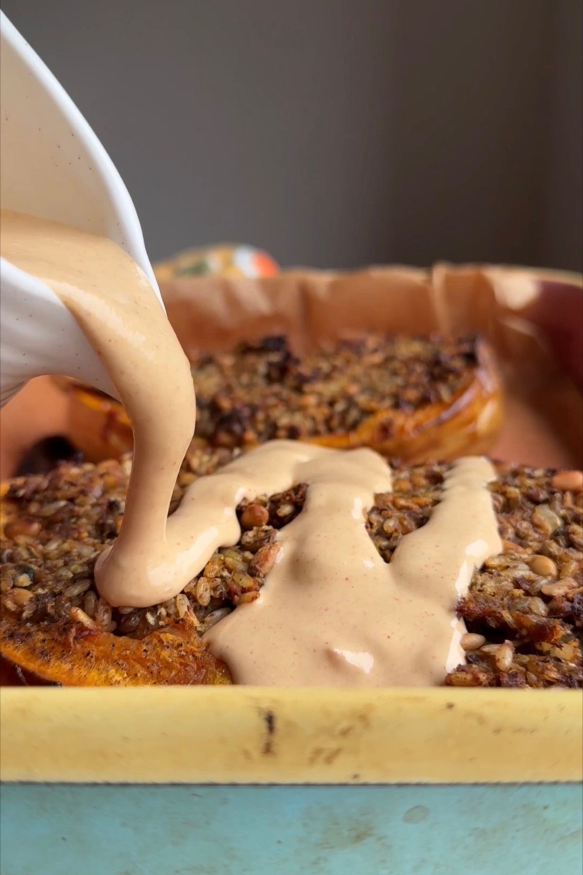 Thick tahini sauce being poured over the stuffed butternut squash.