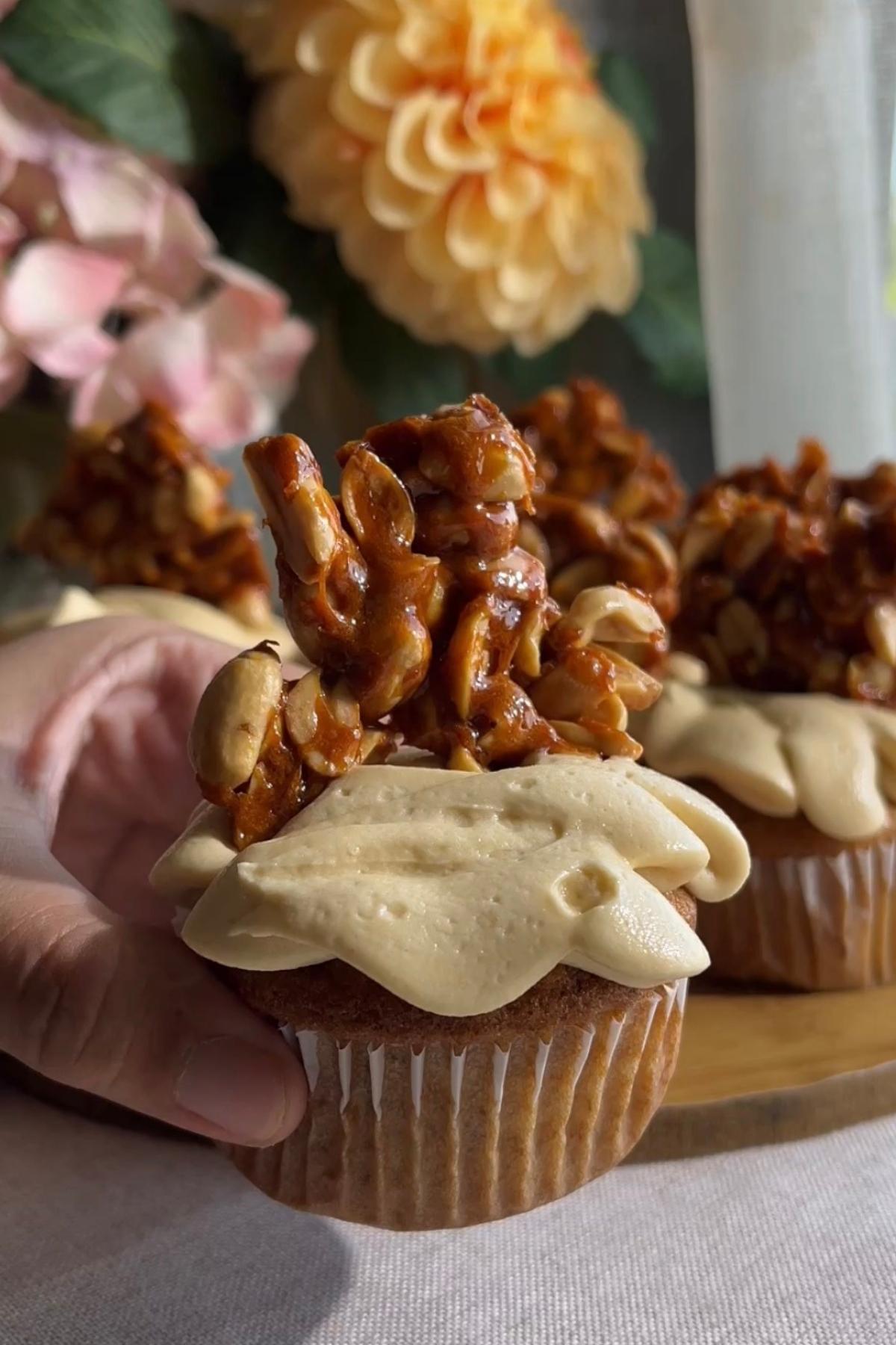 Hand holding a cupcake topped with peanut butter frosting and peanut brittle.