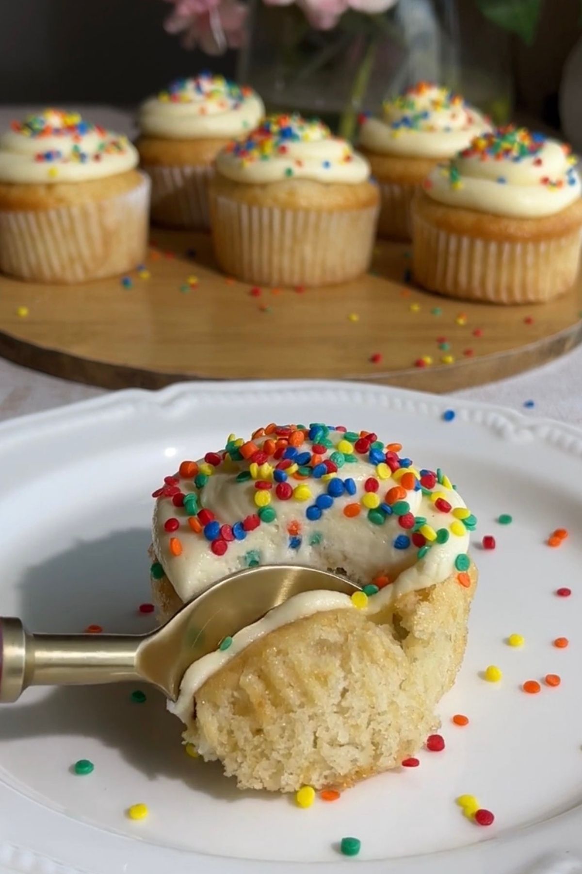 A spoon cutting into a frosted cupcake topped with rainbow sprinkles.