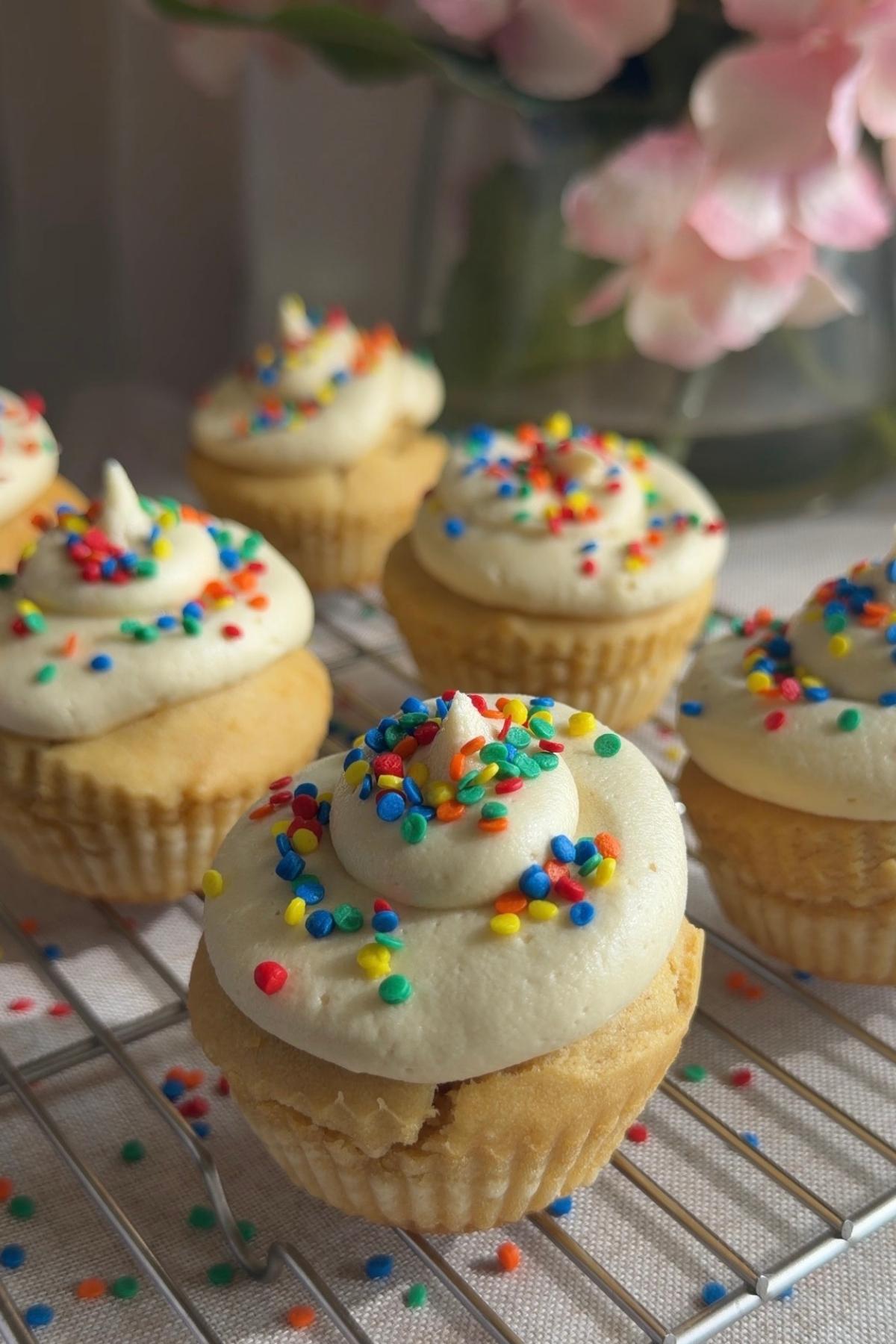 Frosted cupcakes with rainbow sprinkles on a cooling rack.