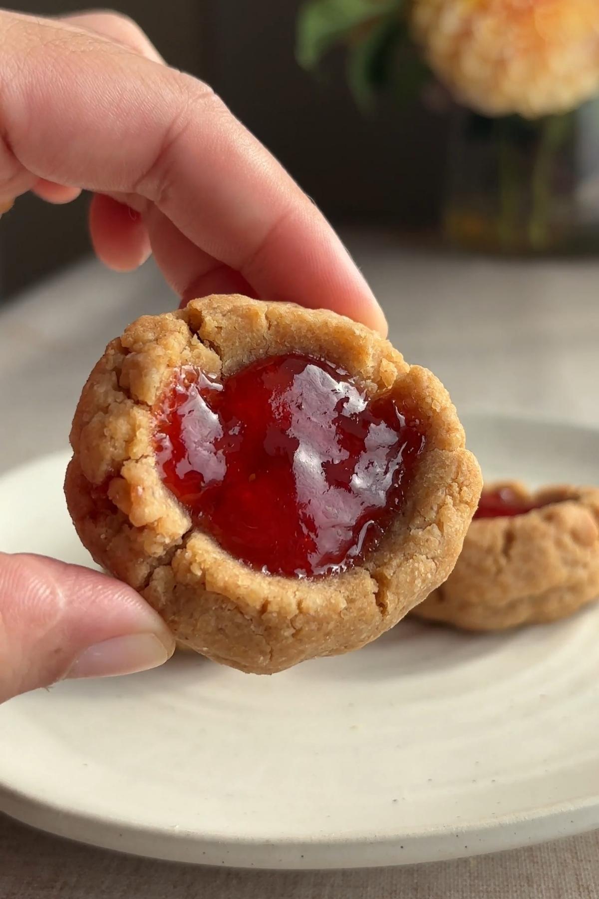 Close-up of an almond butter thumbprint cookie with a glossy strawberry jam center.