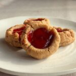 Almond butter thumbprint cookies with glossy strawberry jam on a white plate.