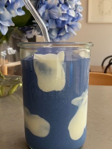 Blue spirulina smoothie with creamy yogurt swirls in a glass jar with a reusable glass straw.