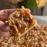 Hand holding a caramel apple crumb bar topped with crumble and caramel drizzle.