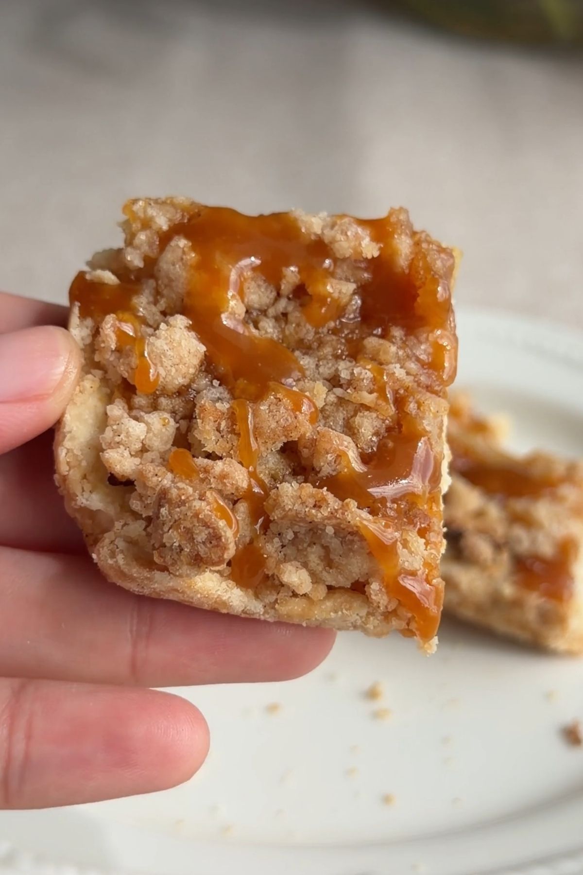Hand holding a caramel apple crumb bar with caramel drizzle.