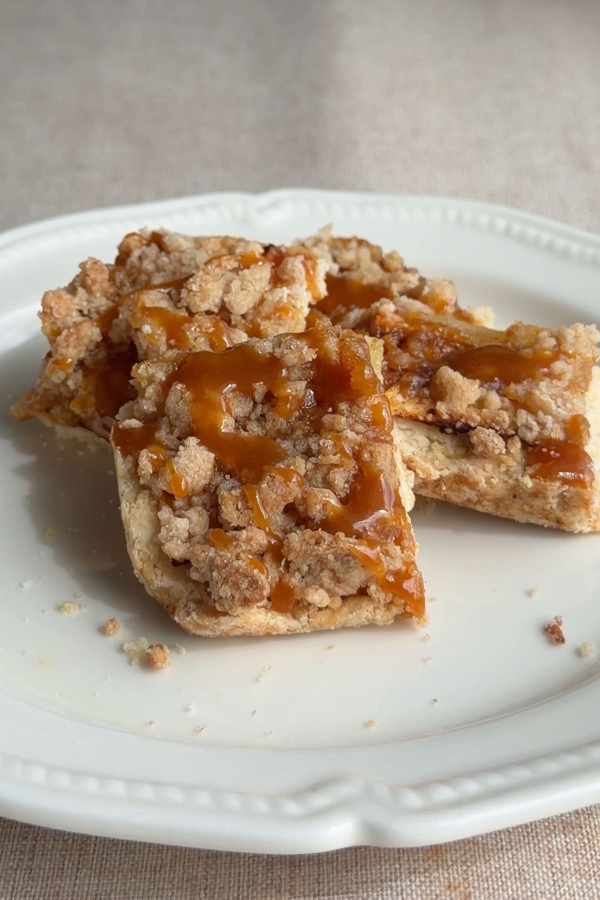 Caramel apple crumb bars stacked on a white plate with caramel drizzle.