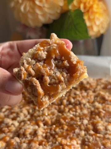 Hand holding a caramel apple crumb bar topped with crumble and caramel drizzle.