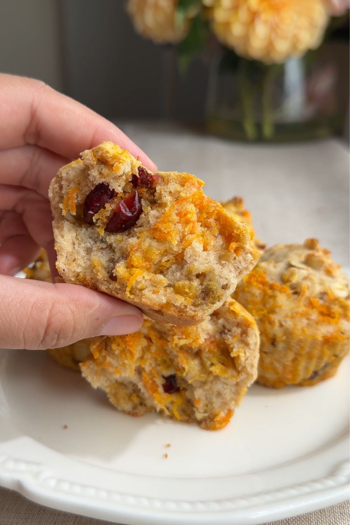Hand holding a broken vegan carrot cake muffin showing the moist crumb and dried cranberries.