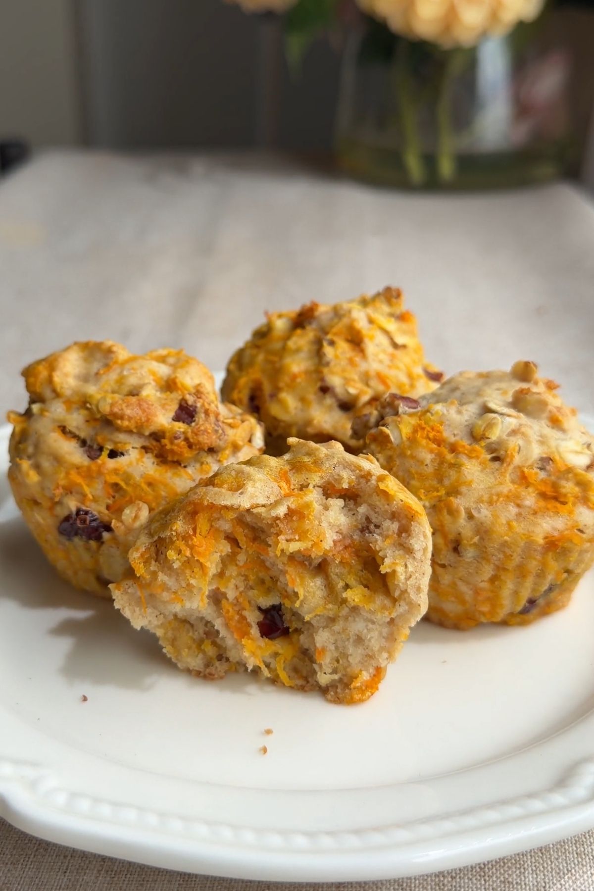Vegan carrot cake muffin broken open to show the soft crumb with carrot, oats, and dried cranberries.