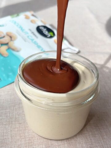 Chocolate sauce being poured over creamy cashew mousse in a glass jar.