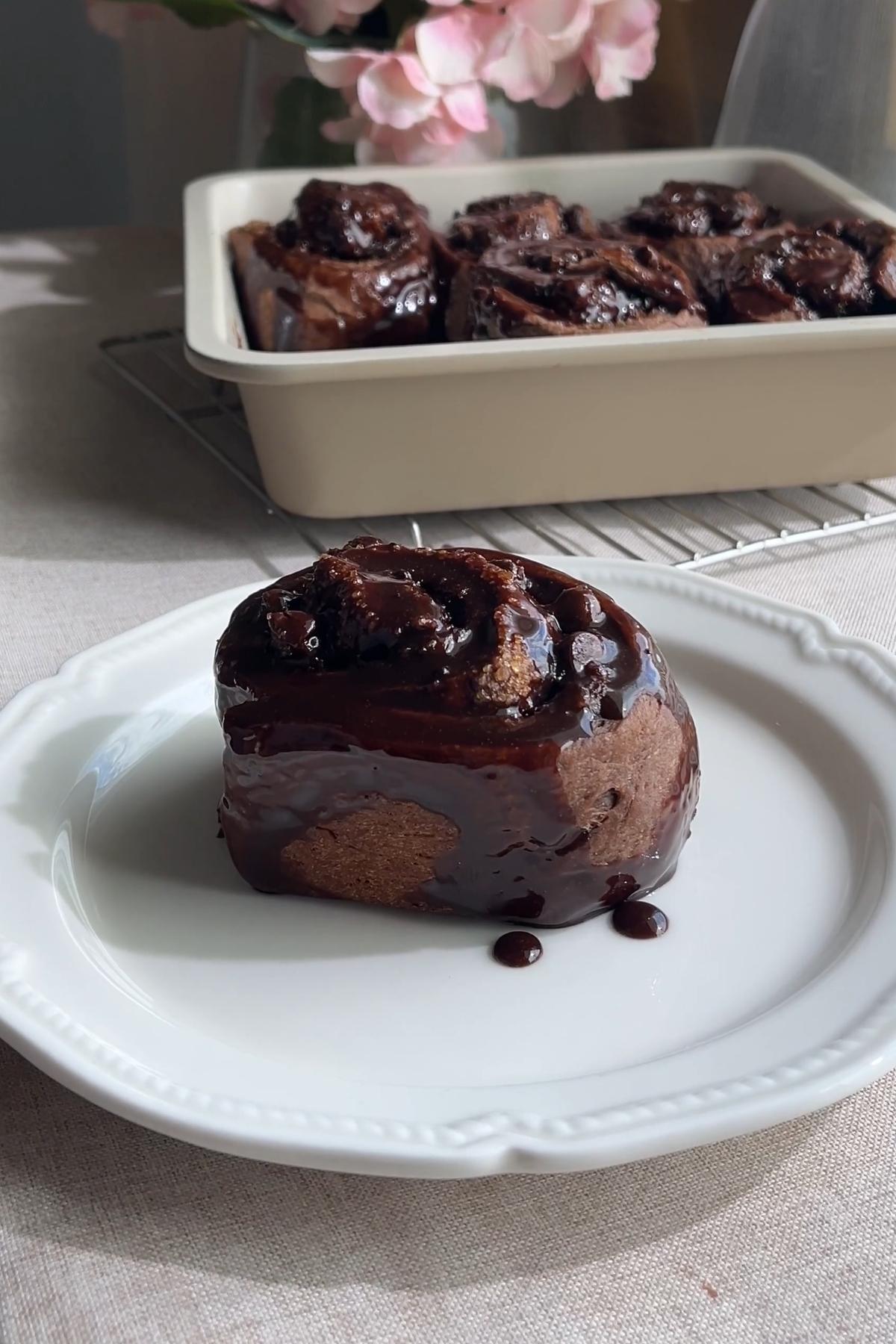 Chocolate cinnamon roll drizzled with rich chocolate glaze on a white plate.