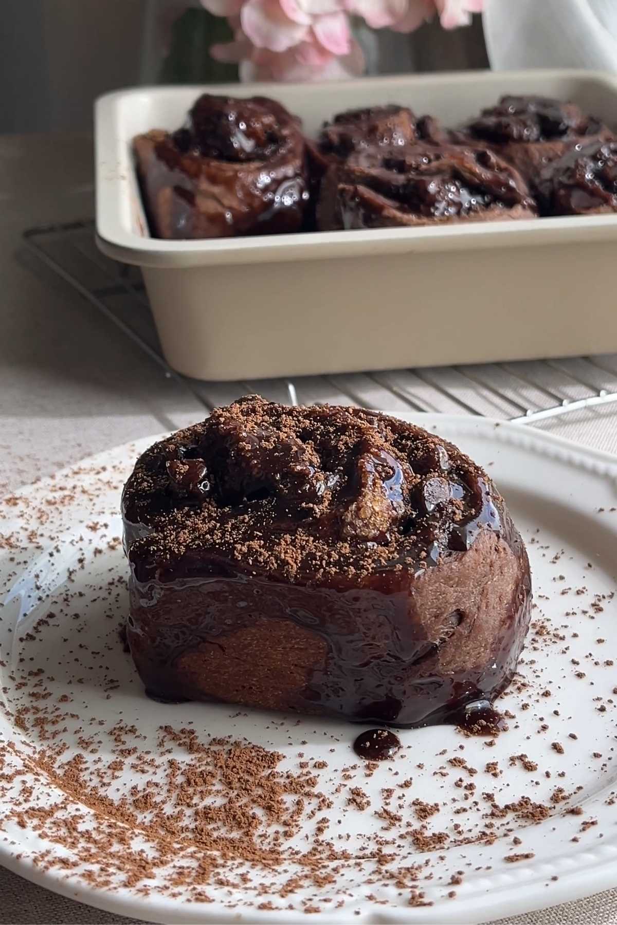 Chocolate cinnamon roll topped with glossy chocolate glaze and cocoa powder.