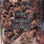Container of chunky chocolate coconut granola with large chocolate pieces and coconut flakes.