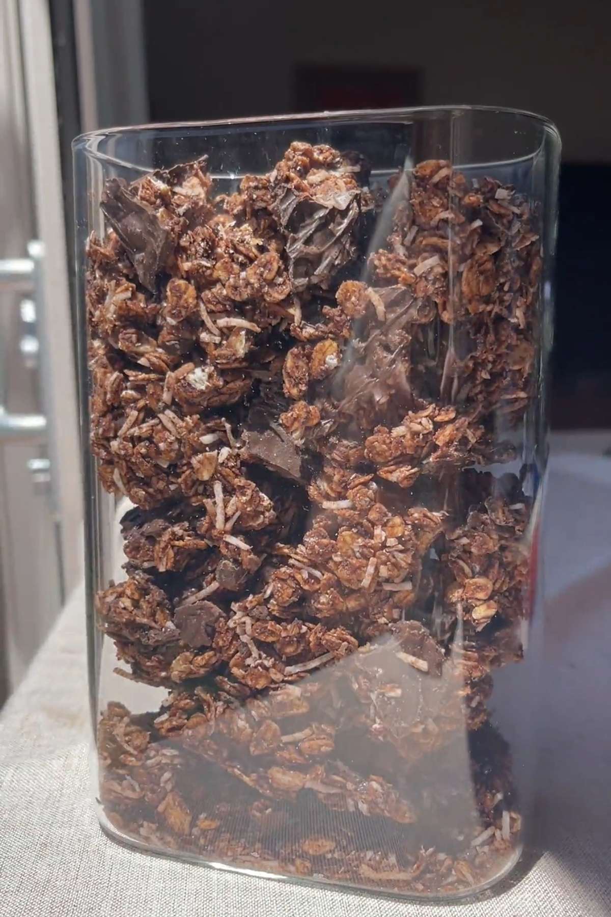 Glass container filled with chunky chocolate coconut granola and large chocolate pieces.