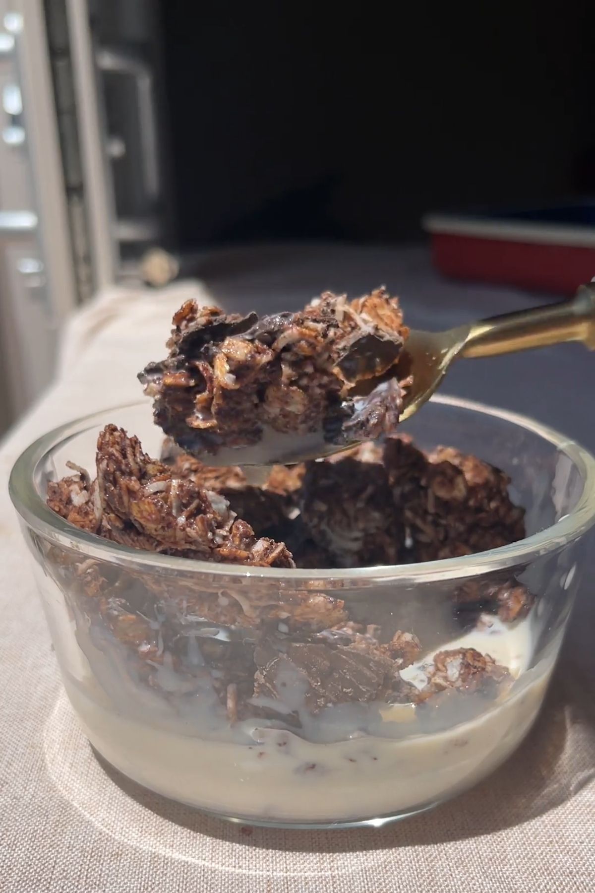 Spoon lifting crunchy chocolate coconut granola from a bowl of plant-based yogurt.