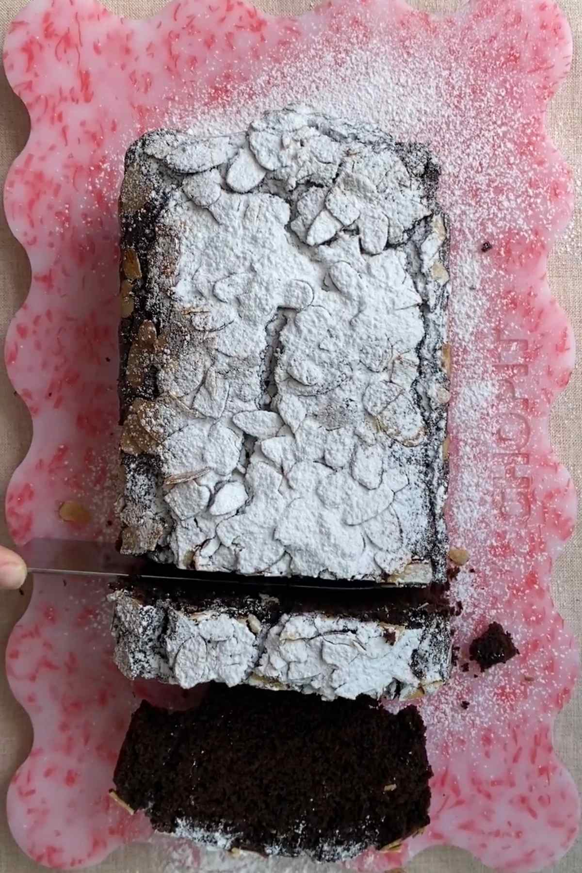 Chocolate olive oil loaf cake dusted with powdered sugar on a pink board.