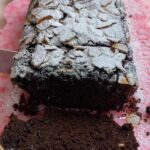 Chocolate olive oil loaf cake dusted with powdered sugar being sliced.