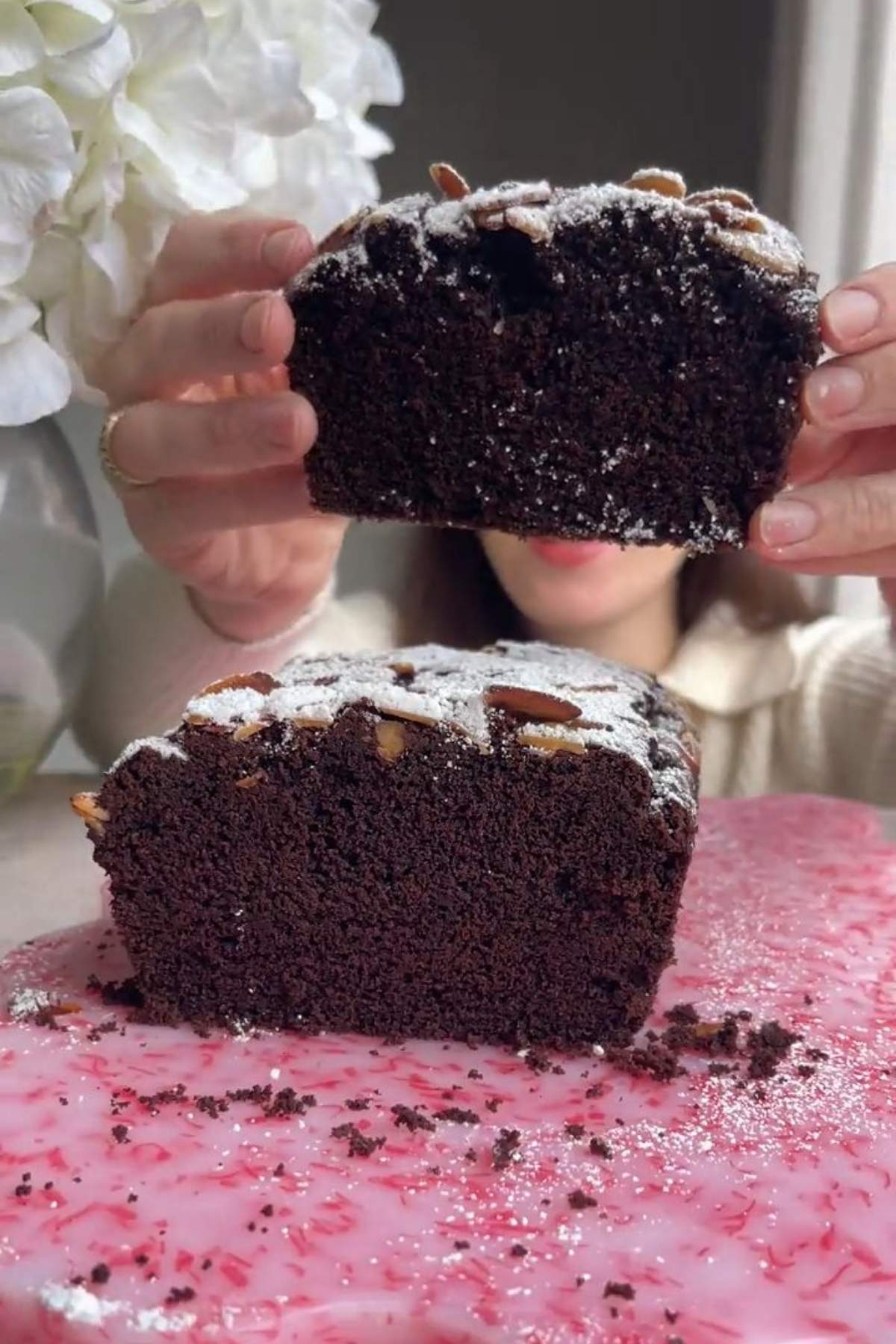 Person holding a slice of chocolate olive oil cake over the loaf.
