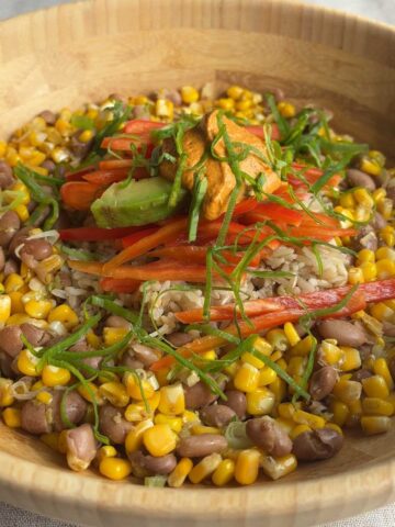 Brown rice bowl topped with avocado, red bell pepper, creamy chipotle dressing, and green onions.