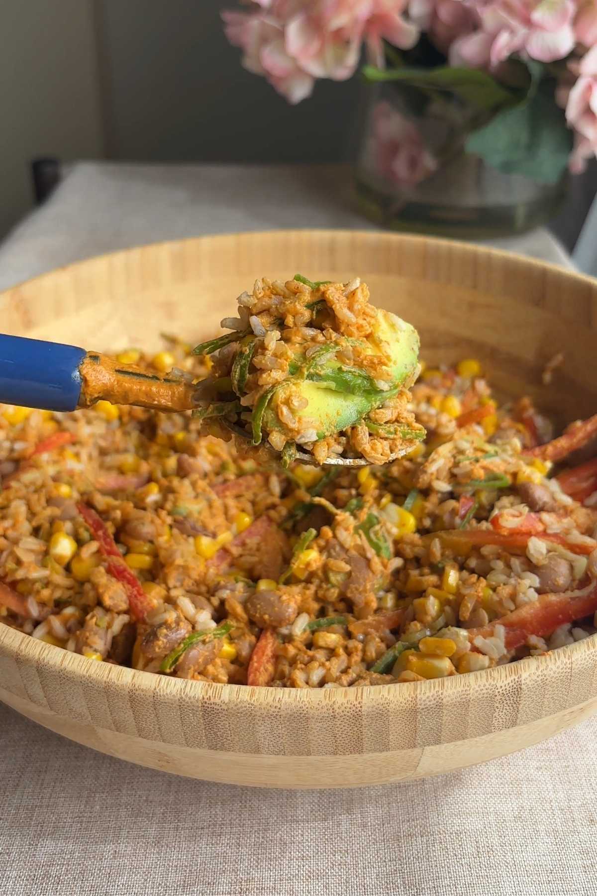 Spoonful of brown rice bowl with avocado, corn, pinto beans, and creamy chipotle dressing.