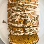 Top-down view of sliced vegan pumpkin bread with maple glaze and pepitas on a white plate.