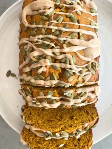 Top-down view of sliced vegan pumpkin bread with maple glaze and pepitas on a white plate.