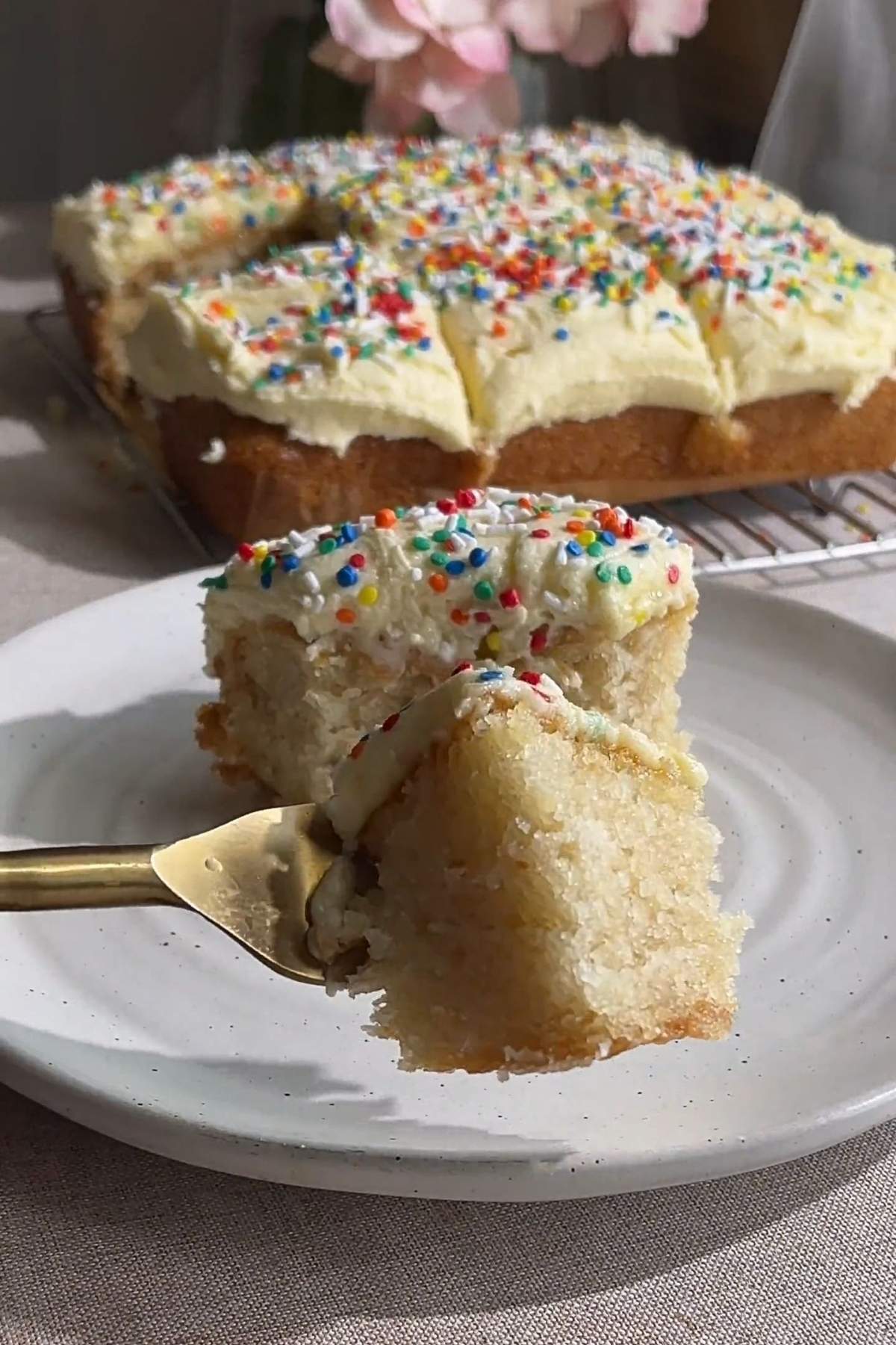 Fork holding a bite of vegan vanilla cake with vanilla frosting and colorful sprinkles.