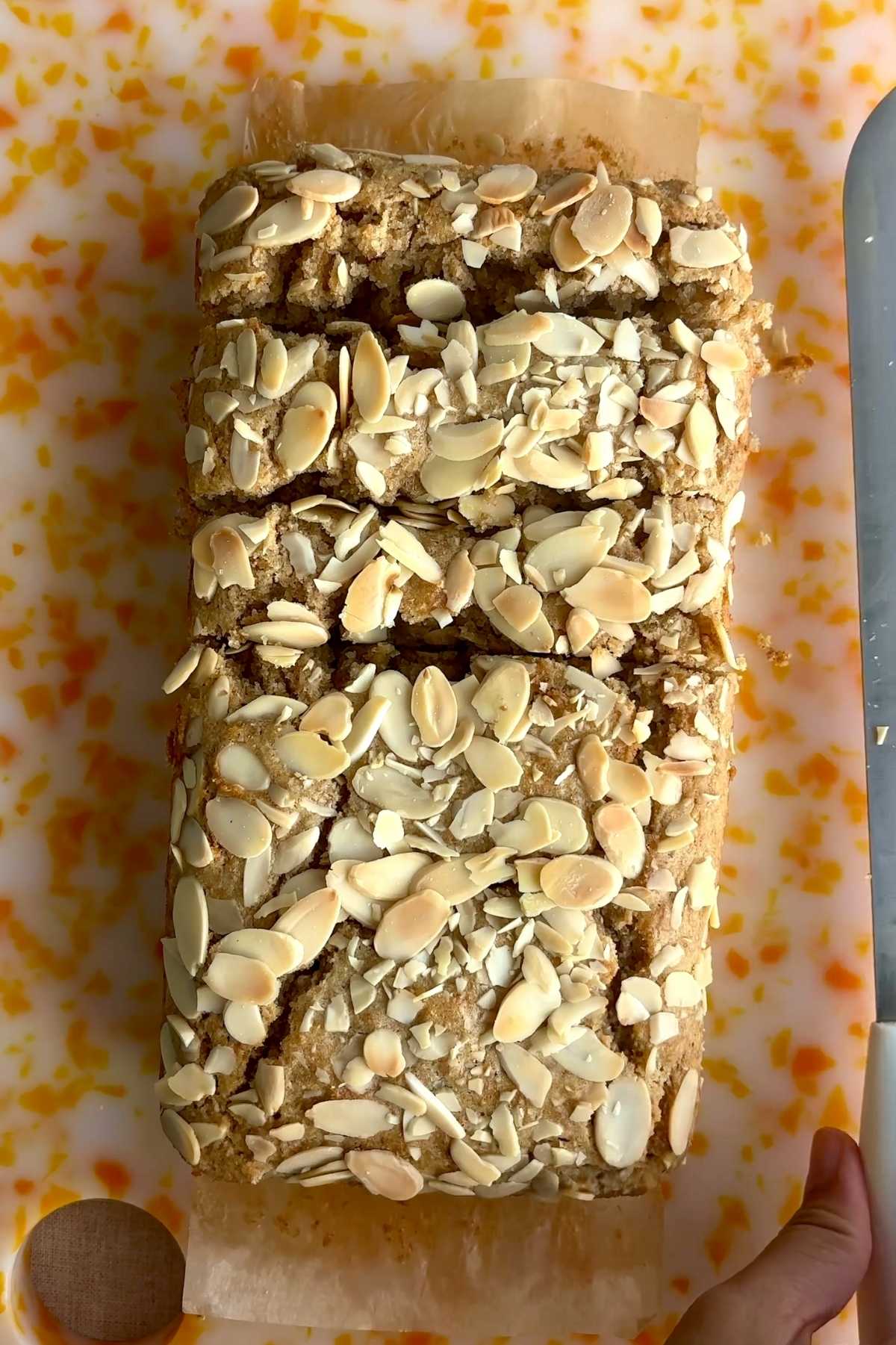 Overhead view of a gluten-free lemon loaf topped with toasted sliced almonds before slicing.