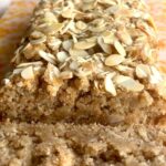 Gluten-free lemon loaf topped with toasted sliced almonds on parchment paper, with one slice cut.