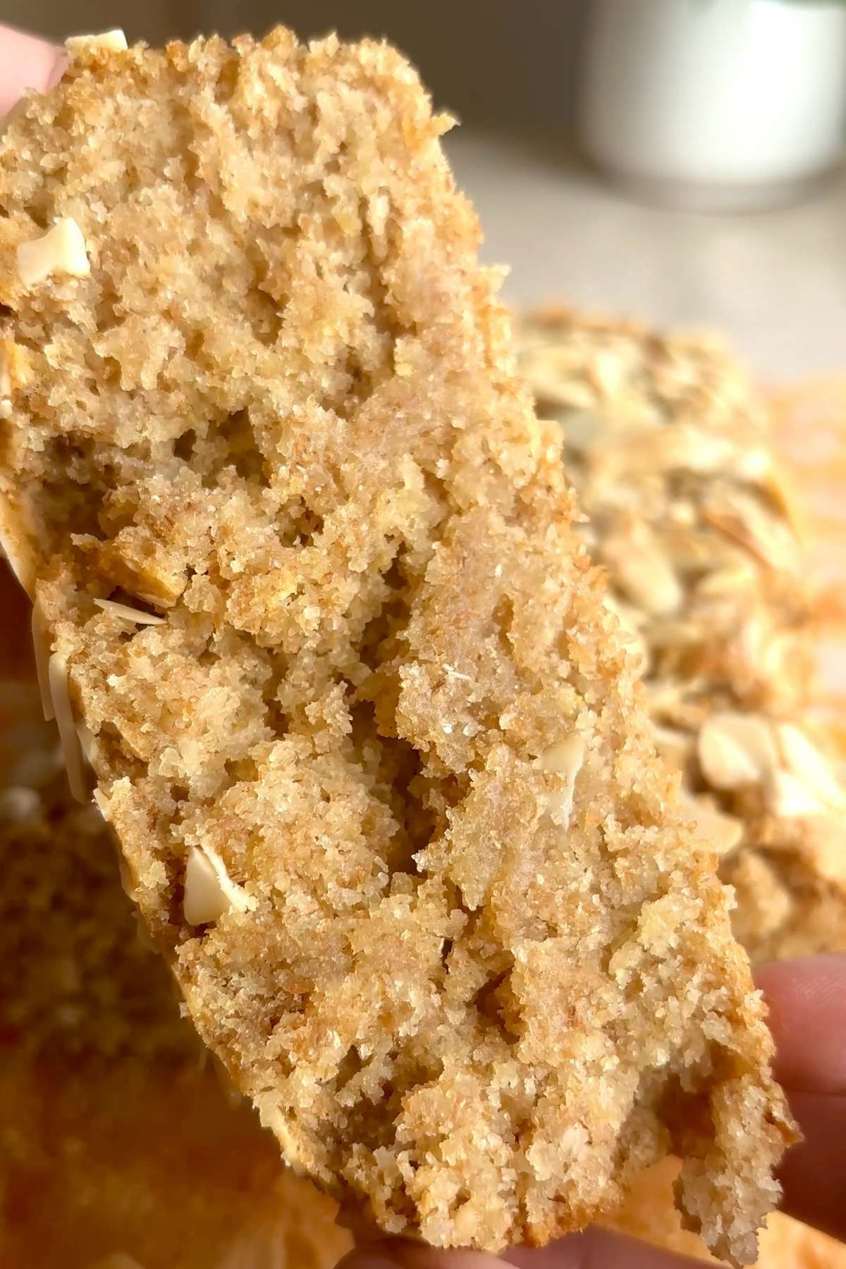 Slice of gluten-free lemon loaf showing a soft, tender crumb with toasted sliced almonds on top.