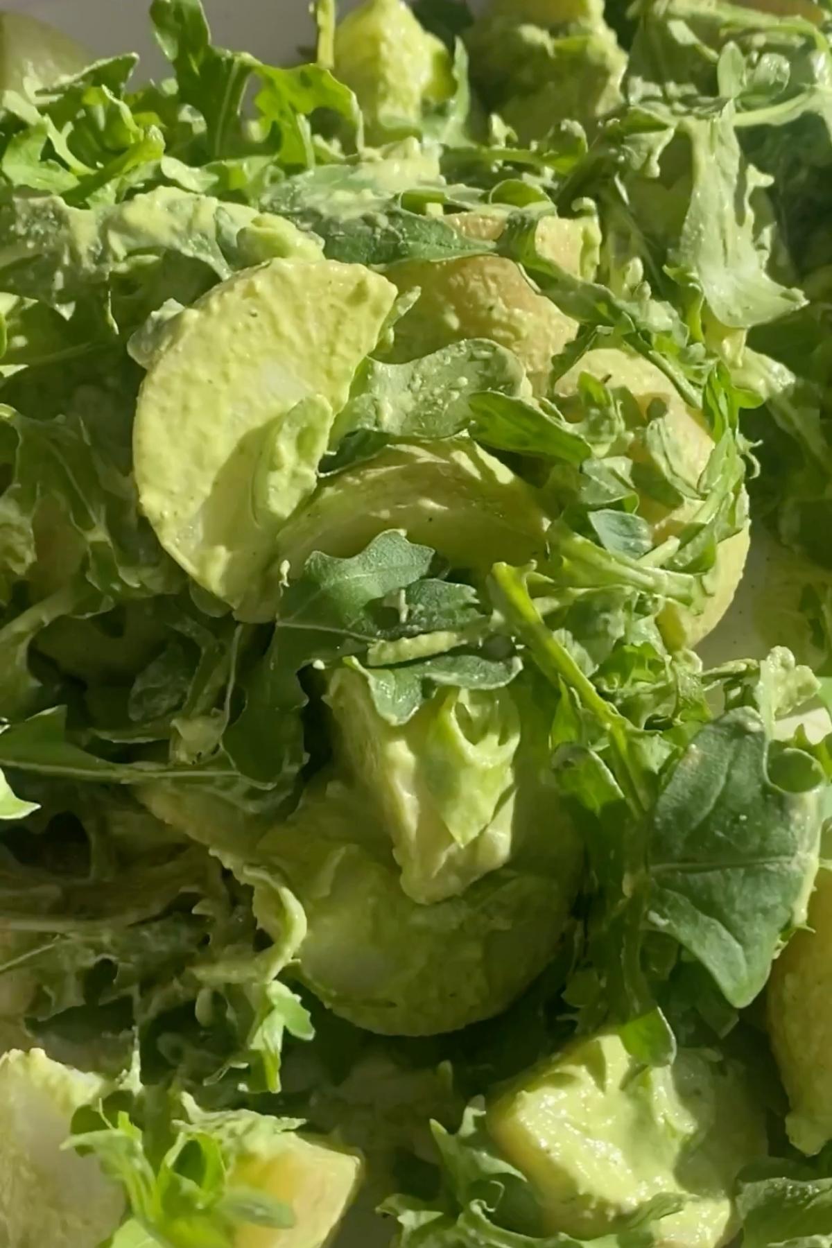 Close-up of creamy green potato salad with avocado chunks and fresh arugula.