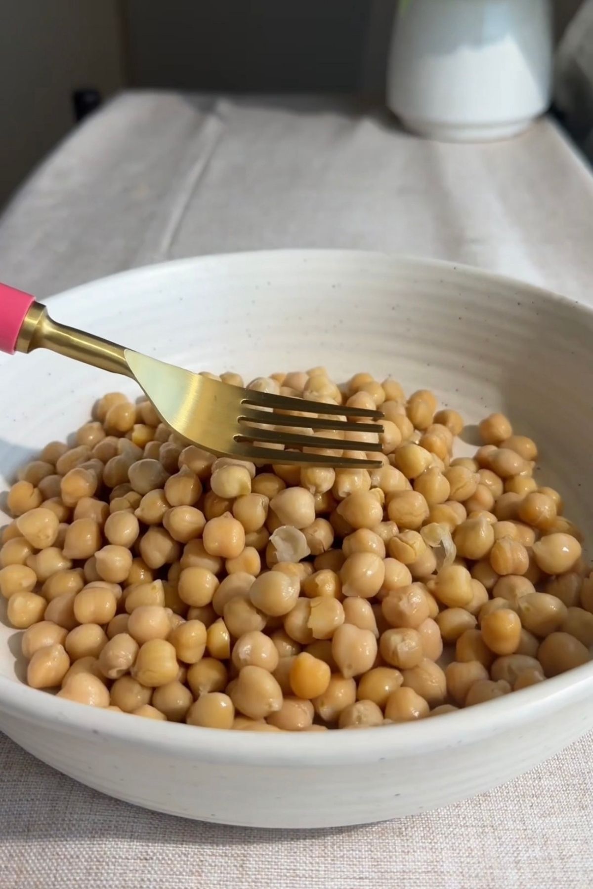 Drained chickpeas in a yellow bowl on a light tablecloth.
