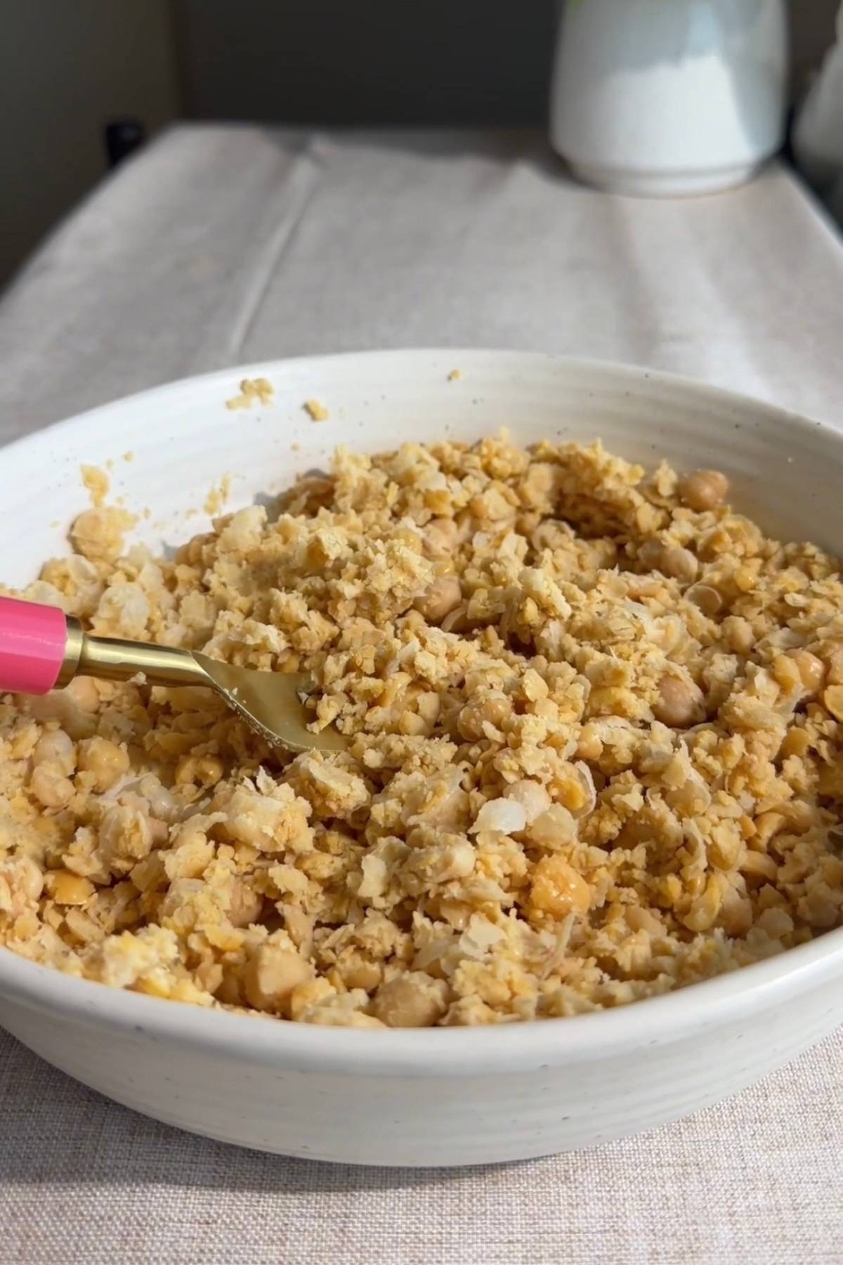 Hand using a fork to mash chickpeas in a yellow bowl.