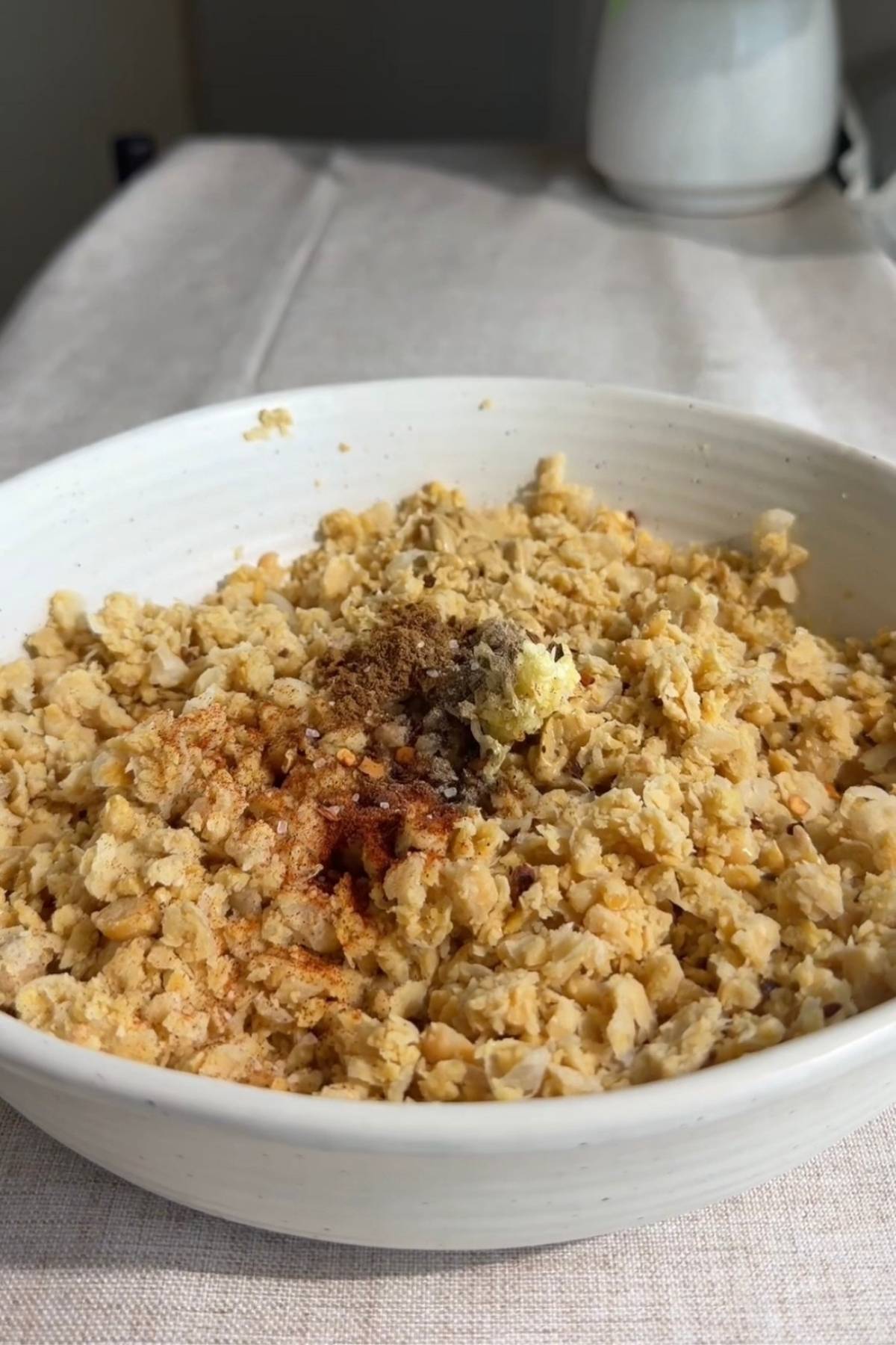 Mashed chickpeas topped with mustard, spices, and salt in a yellow bowl.