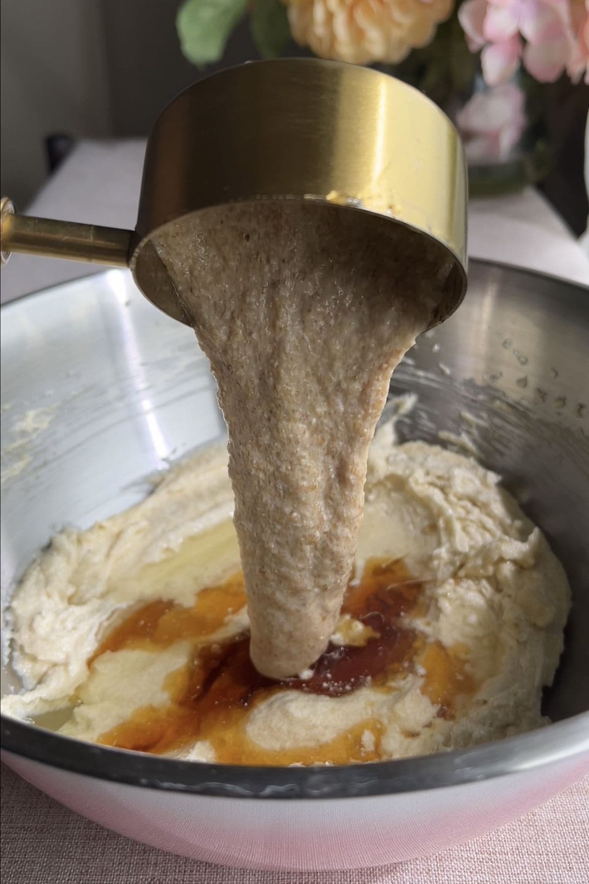 Wet ingredients poured from a gold measuring cup into the creamed mixture.