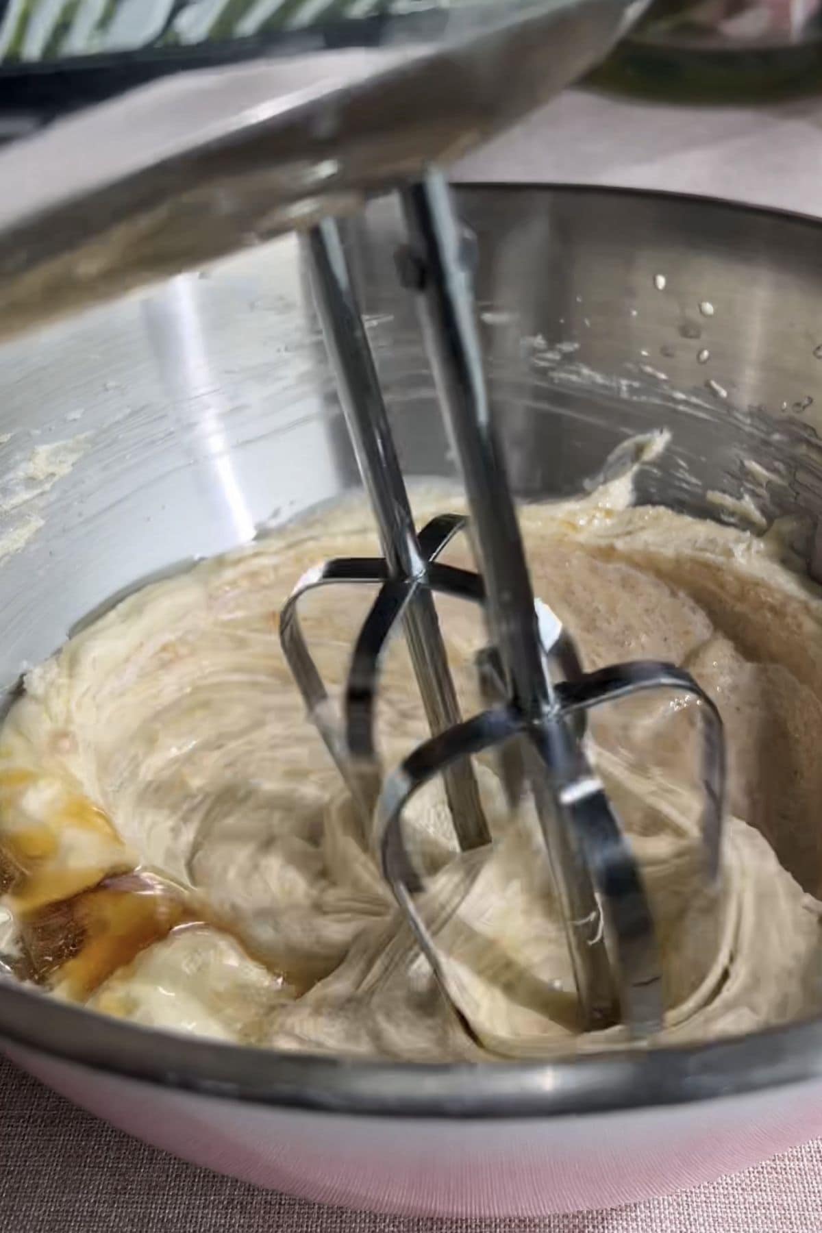 Electric beaters mixing wet ingredients into the pale creamed mixture.
