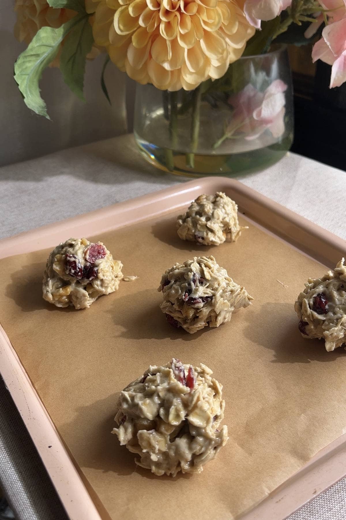 Six scoops of cookie dough spaced on a parchment-lined pink baking tray.