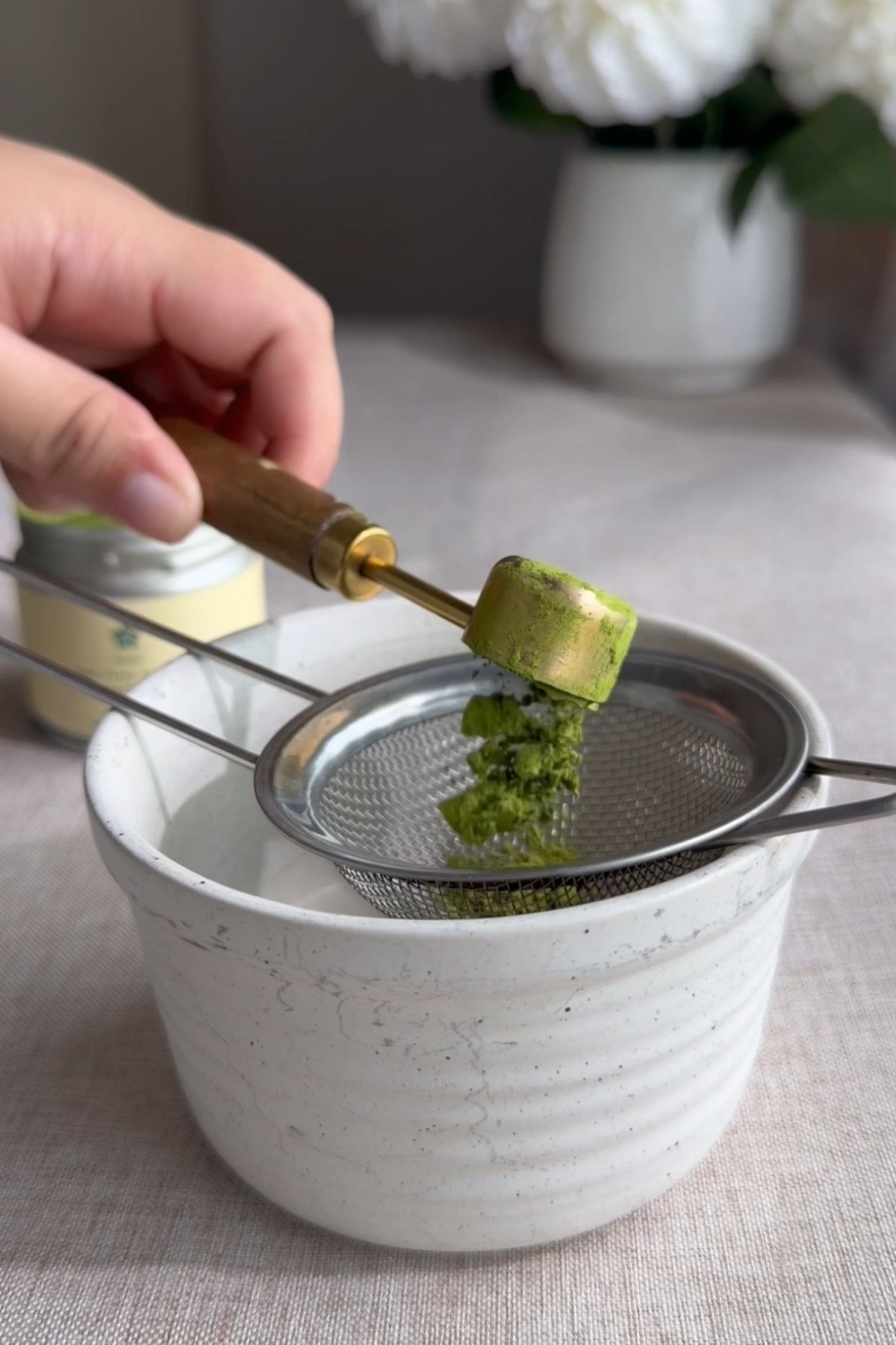 Matcha being pressed through a small sieve into a bowl.