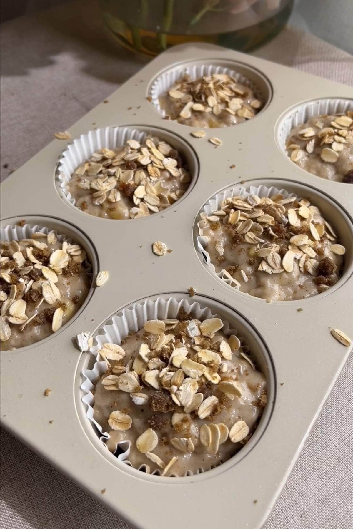 Muffin batter in paper-lined cups topped with rolled oats and sugar.