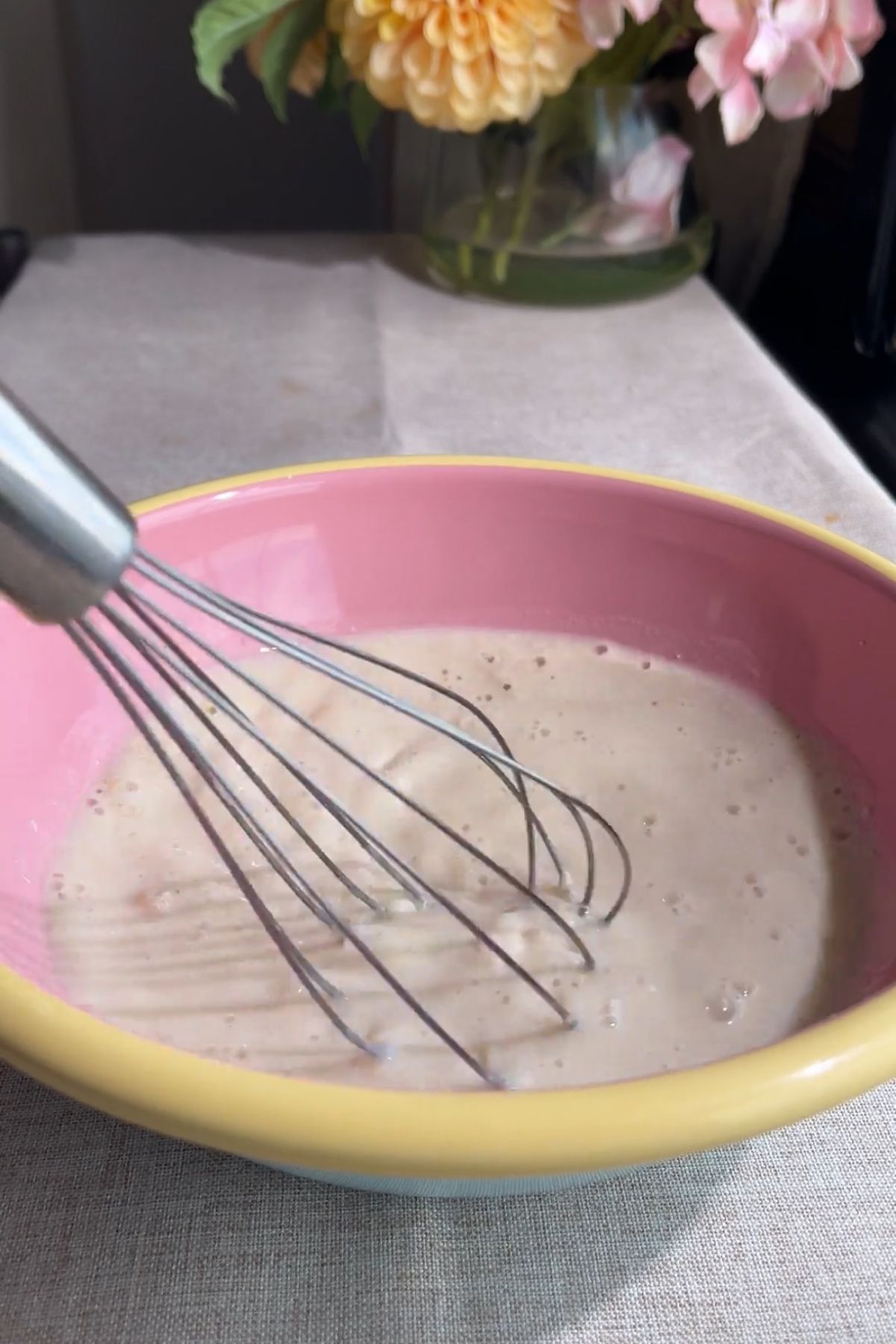Whisk mixing a foamy milk and yeast mixture in a pink bowl.