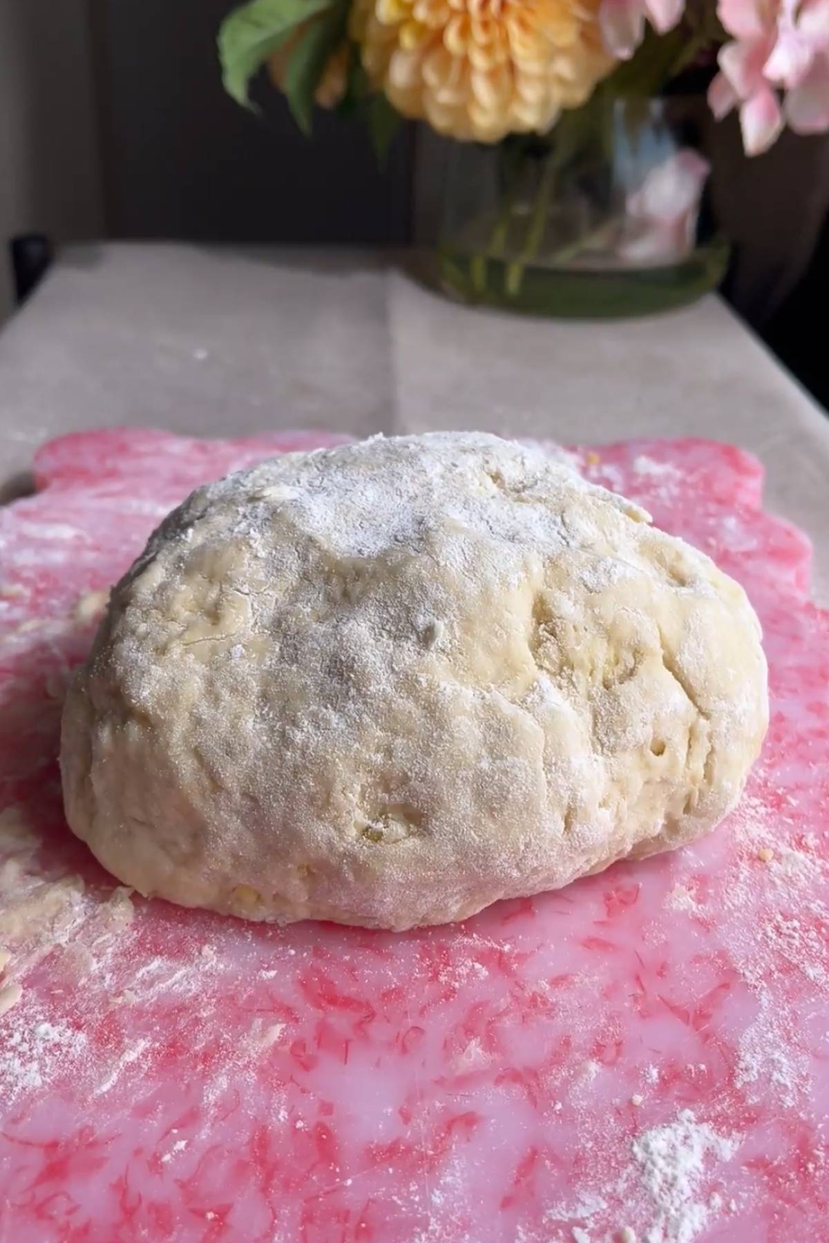 Smooth dough ball dusted with flour on a pink board.