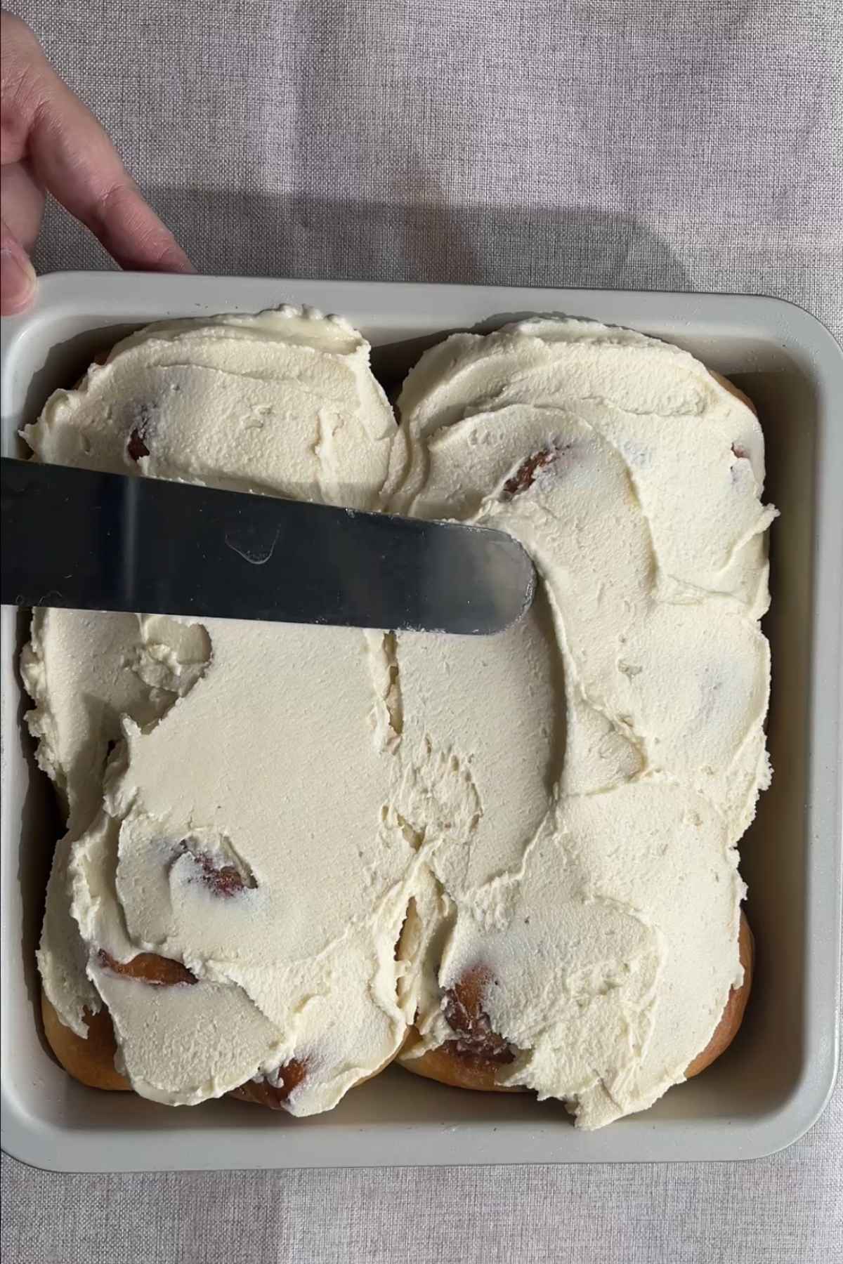 Thick frosting being spread over baked cinnamon rolls.