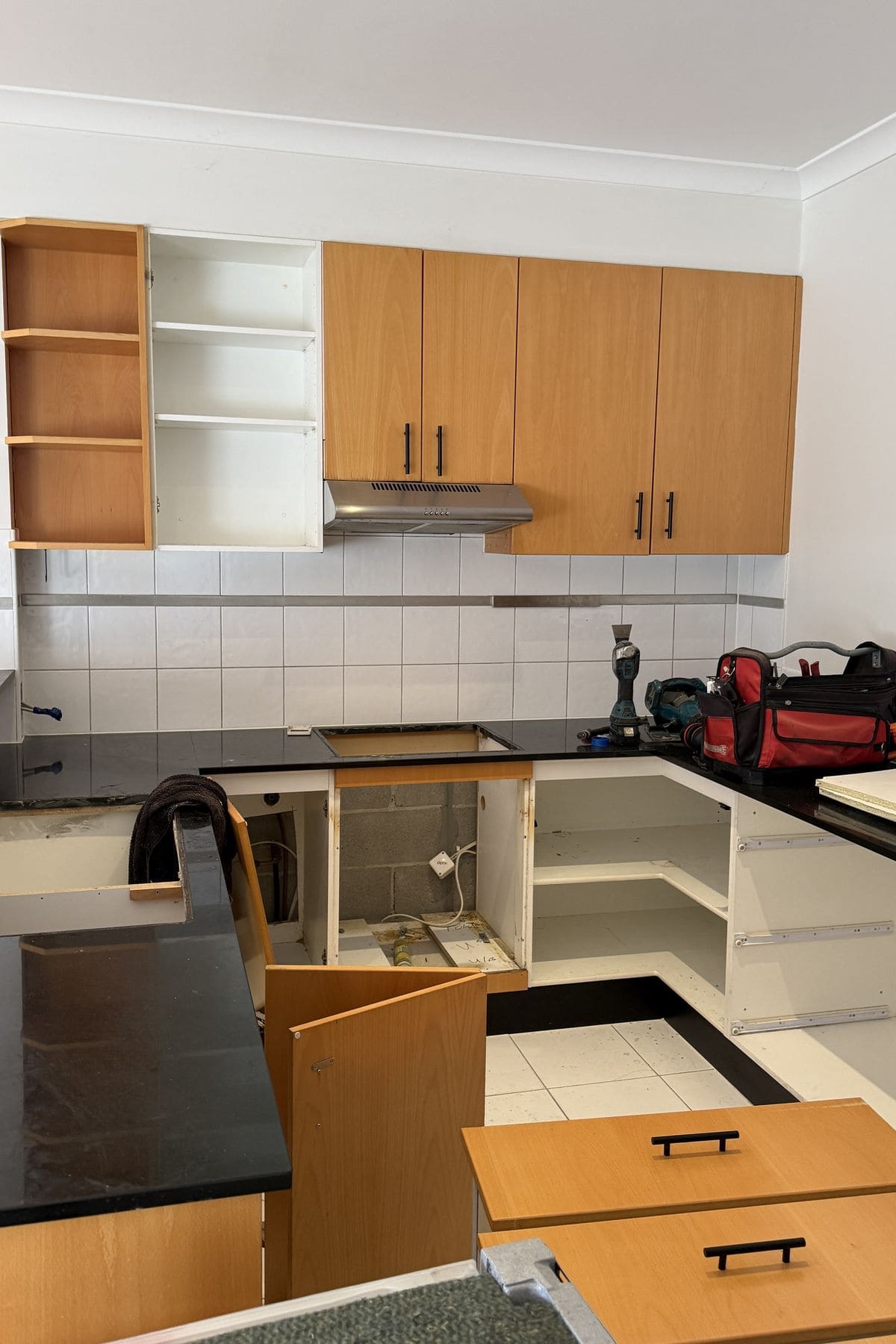 Timber kitchen cabinets with the doors removed and a black stone benchtop still in place.